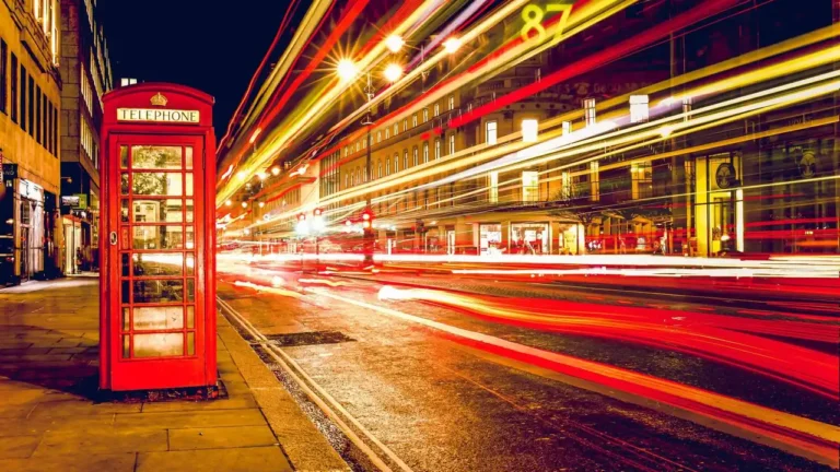 A red London telephone box beside a street at night with car light trails