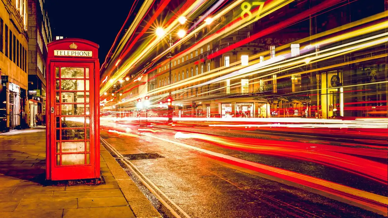 A red London telephone box beside a street at night with car light trails