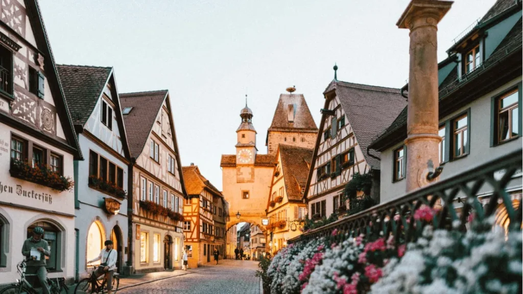 A cobbled street of half-timbered German houses with a clock tower at dusk