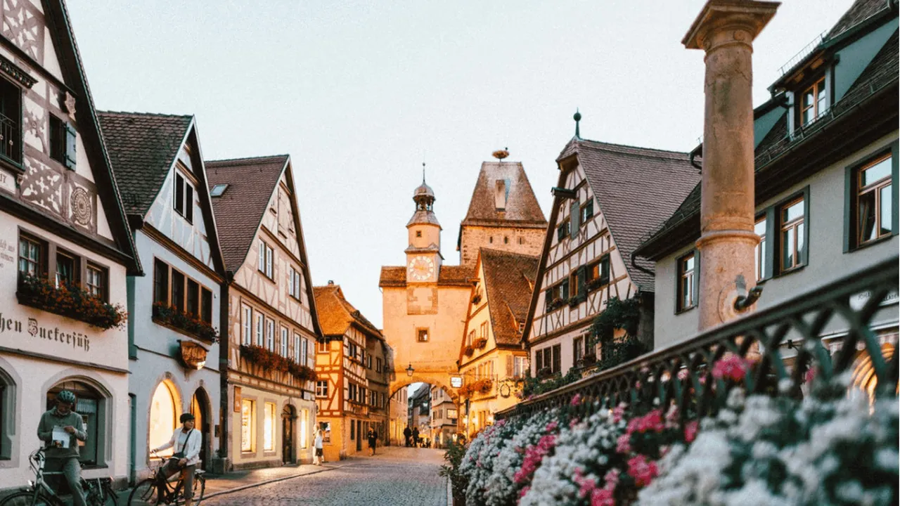 A cobbled street of half-timbered German houses with a clock tower at dusk