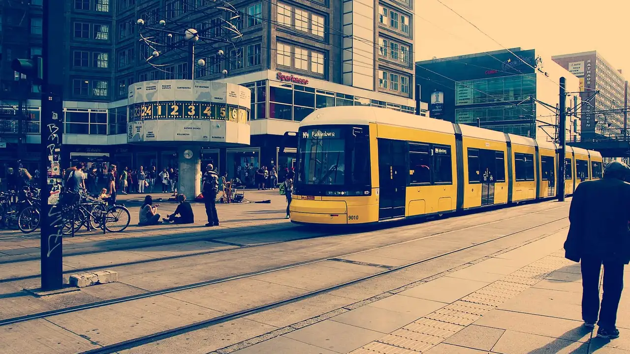 A yellow tram at a city stop with a pedestrian walking along the platform