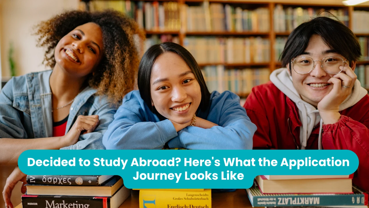 Banner reading 'Decided to Study Abroad? Here's What the Application Journey Looks Like' across a photograph of three smiling students leaning on a library table stacked with dictionaries and textbooks in front of full bookshelves