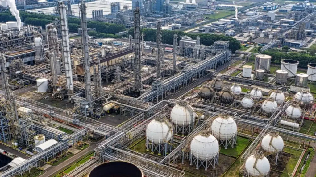 An aerial view of a chemical processing plant, with distillation columns, pipe racks and rows of white spherical storage tanks.