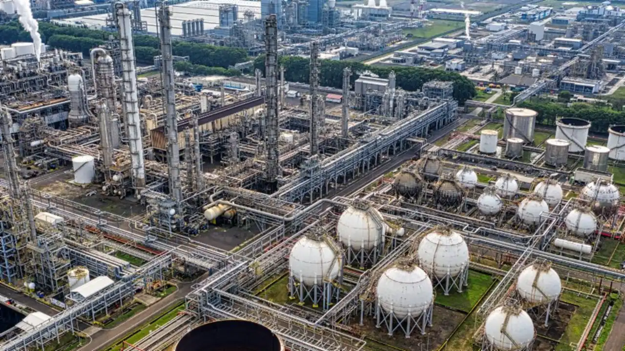 An aerial view of a chemical processing plant, with distillation columns, pipe racks and rows of white spherical storage tanks.