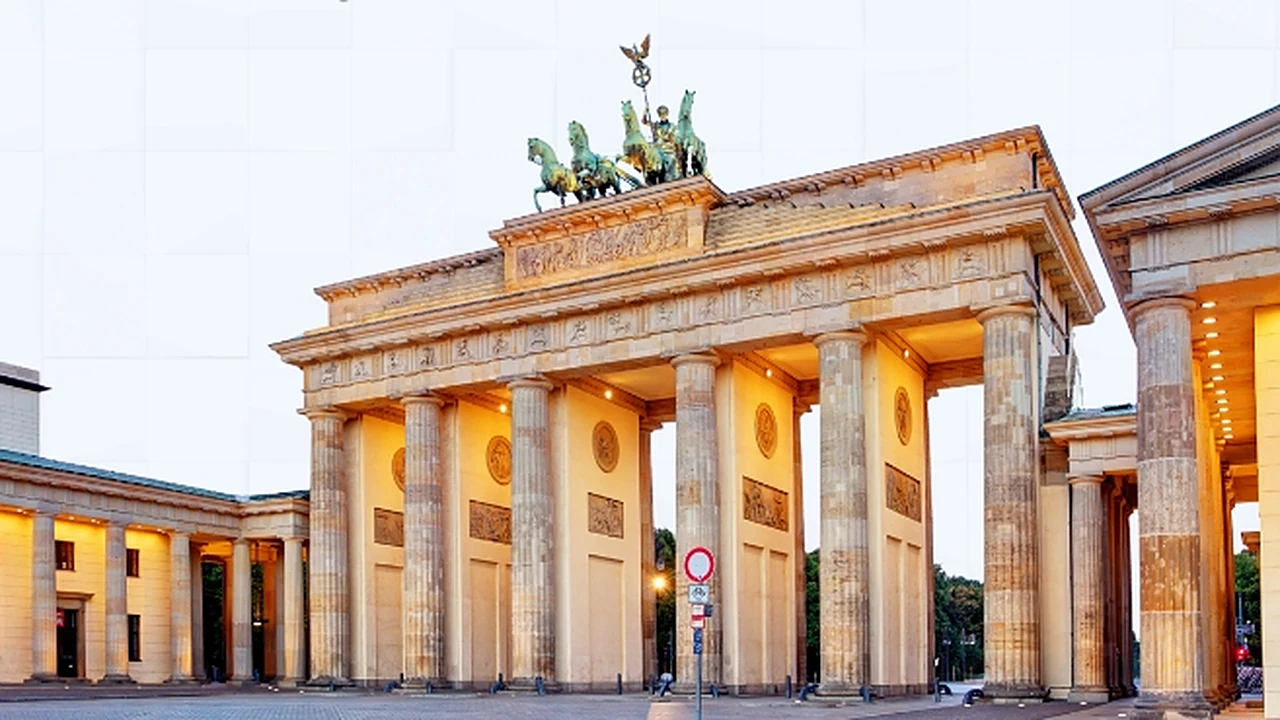 The Brandenburg Gate in Berlin lit at dusk, its columns and the bronze quadriga statue on top seen from the square in front of it.