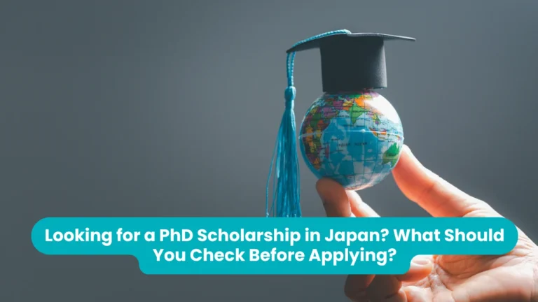 Banner reading 'Looking for a PhD Scholarship in Japan? What Should You Check Before Applying?' across a photograph of a hand holding up a small globe topped with a miniature graduation cap and a blue tassel, against a grey background