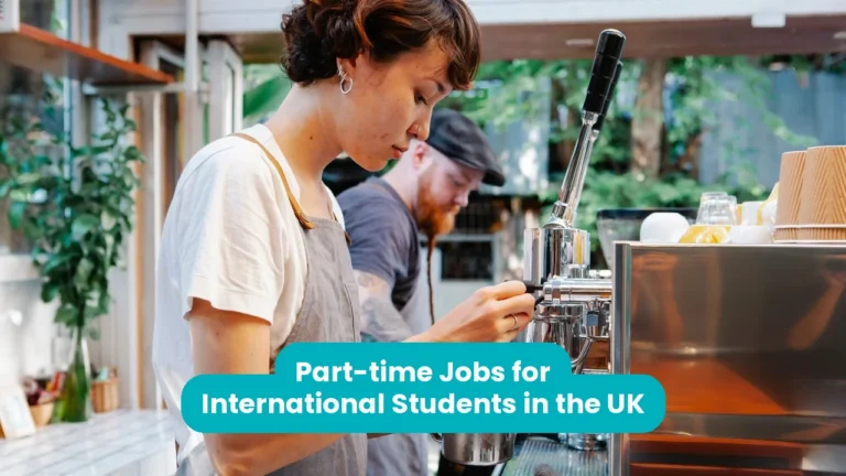 A young barista in a white T-shirt and grey apron steams milk at a chrome espresso machine, while a second barista works behind her in a bright cafe with green plants. A teal banner across the lower third reads ‘Part-time Jobs for International Students in the UK’.